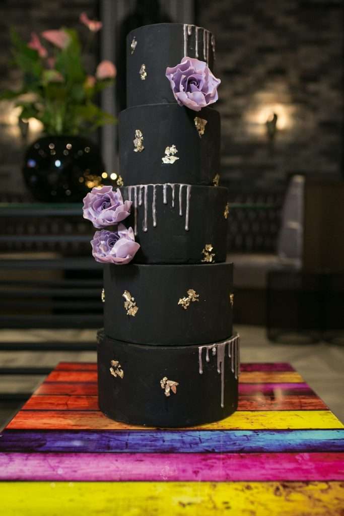 Five tier black wedding cake with gold drips and purple sugar flowers at The Courthouse Hotel, Shoreditch
