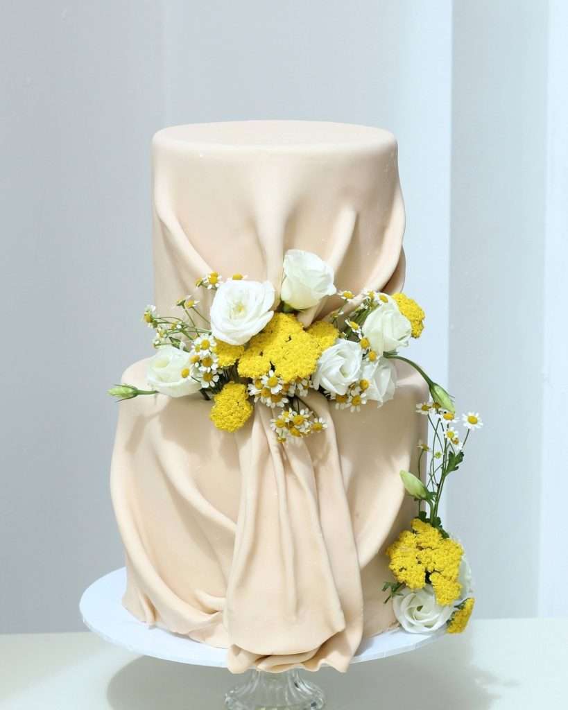 Two tier fondant drape cake with daisies and fresh flowers