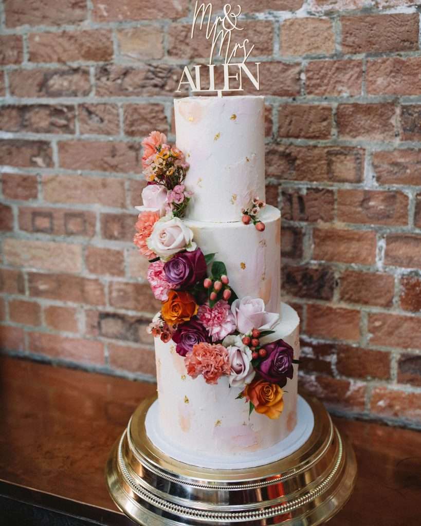 Painted buttercream peach and blush wedding cake with fresh flowers in peach, purple, pink and blush