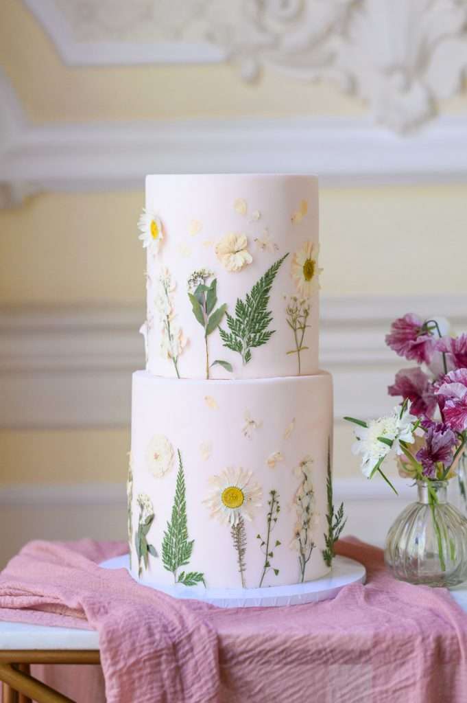 Two tier pink wedding cake with green and white pressed flowers